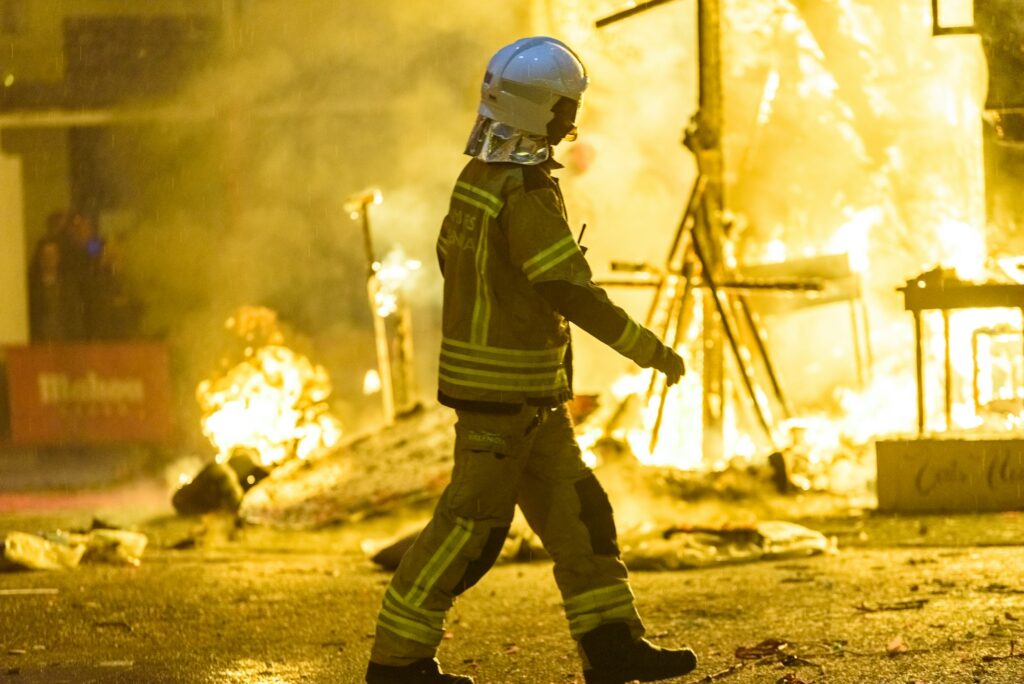 Firemen around a bonfire caused by a Falla Valenciana controlling the flames of the fire.